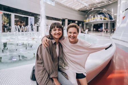 Two girls have fun in the mall, a fountain in the background