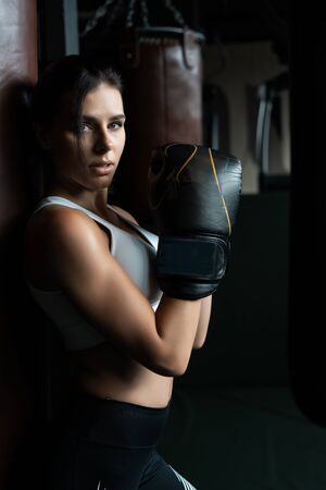 Boxing woman posing with punching bag, on dark background. Strong and independent woman conceptの写真素材