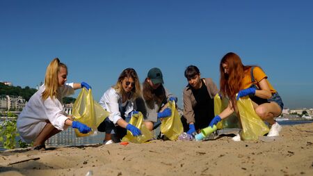 Group of activists friends collecting plastic waste on the beach. Environmental conservation.