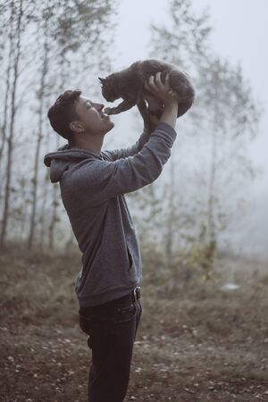 The guy holds a cat in the park. The park is shrouded in fogの写真素材