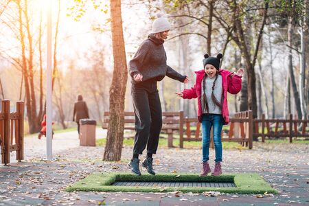 Mom and her daughter jumping together on trampoline in autumn parkの写真素材