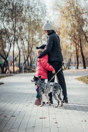 Happy mother and her daughter walk with dog in autumn parkの写真素材