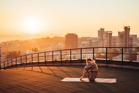 Woman doing yoga on the roof of a skyscraper in big city. Sunsetの写真素材