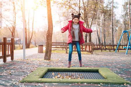 Happy school girl jumping on a small trampoline in the parkの写真素材