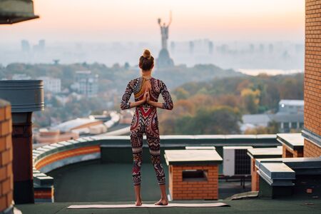 Woman doing yoga on the roof in big city.の写真素材