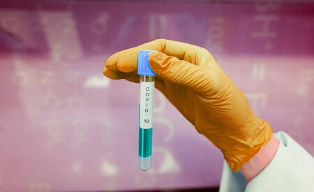 A rubber-gloved hand holds one test tube with coronavirus