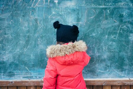 Little girl in autumn park stands at the school board.