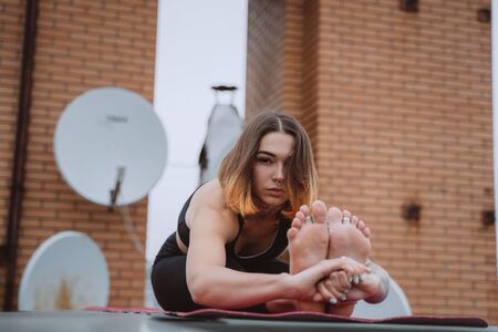 Woman practicing yoga on the mat on the roof and doing yoga exercisesの写真素材