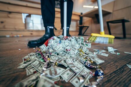 Broom sweeping dollars in scoop from on wooden floorの写真素材