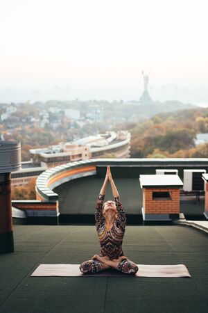 Woman doing yoga on the roof in big city.の写真素材