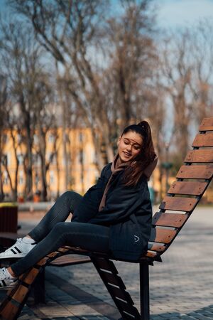 young woman sitting on bench in park, smiling and looking into the cameraの写真素材