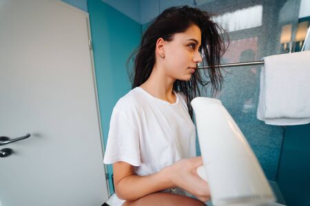 Portrait of young woman using hairdryer in bathroomの写真素材