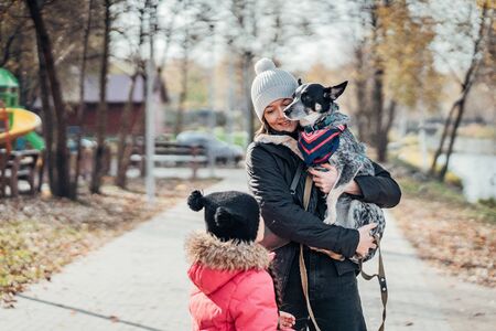 Happy mother and her daughter playing with dog in autumn parkの写真素材