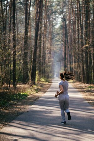 Beautiful young woman running in green park on sunny summer dayの写真素材