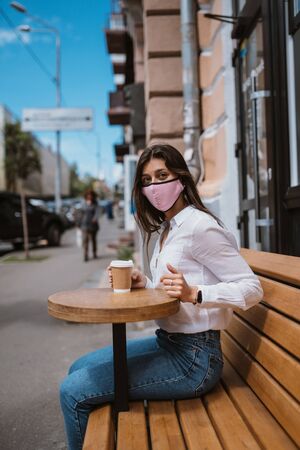 Woman in a medical mask drinks coffee on the streetの写真素材