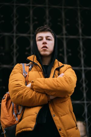 Young adult man in a yellow jacket walks on a city streetの写真素材