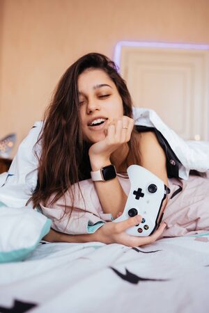 Funny girl lying in bed and playing video game, holding controller