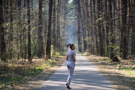 Beautiful young woman running in green park on sunny summer dayの写真素材