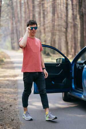 Handsome man standing on the road near opened door of his car.