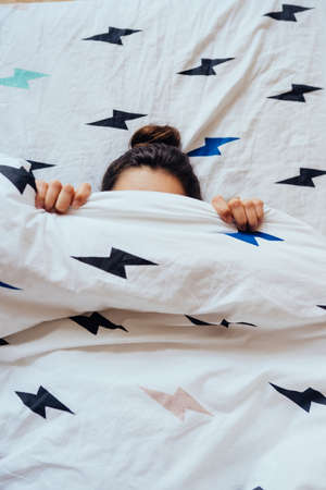 Closeup of Lovely young Woman Lies in Bed Covered with Blanket.の写真素材