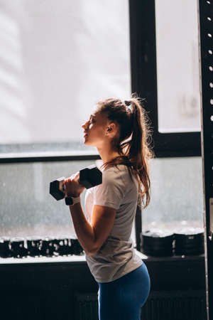 Slender athletic girl performs physical exercises with dumbbells.の写真素材