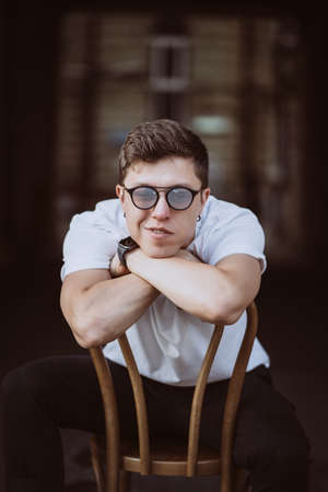 portrait of men sitting on chair with white t-shirt and sunglasses in the street