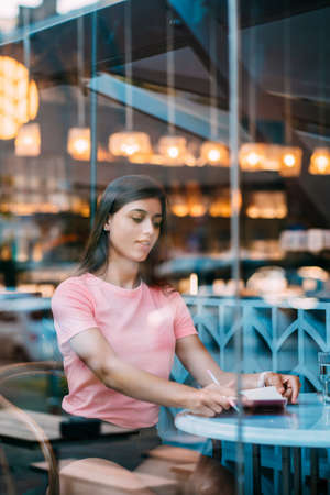 Beautiful brunette sitting behind a window in a cafe bar.の写真素材