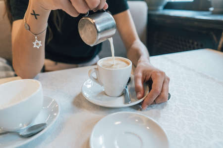 Close-up, hands of a young girl, pours cream or milk into coffeeの写真素材