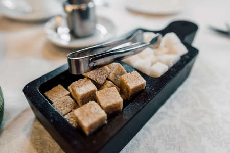 Bowl with pieces of white and brown sugar cubes and with sugar-tongs.の写真素材