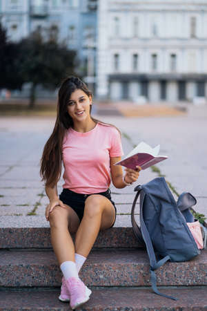 Cheerful young woman taking notes while sitting on steps otdoors