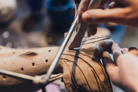 Close-up view of female hands gently handling a clay whale in workshop.