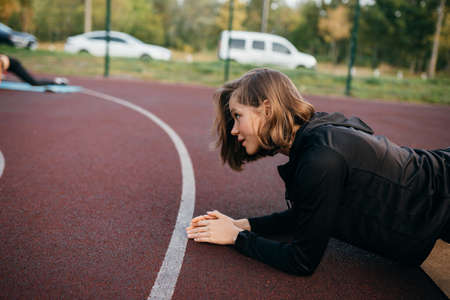 Young fit woman in sportswear trains outdoors on the playground.