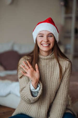 Portrait of friendly brunette woman in santa hat waving raised handの写真素材