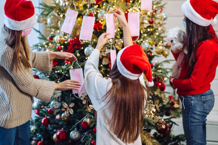 Girls decorate the Christmas tree with protective masks.