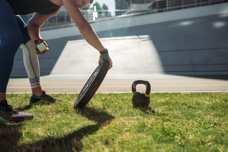 Young guy raises iron plate in the stadium, outdoor workoutの写真素材