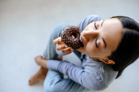 Portrait of rejoicing woman eats tasty donut at home.