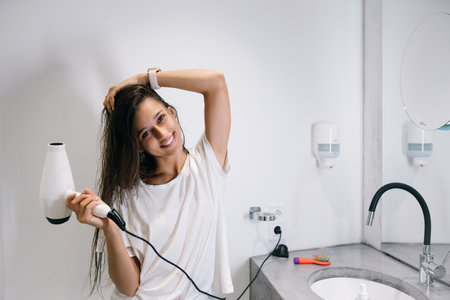 Young beautiful woman in the bathroom holding a hairdryerの写真素材