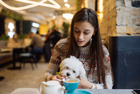 Beautiful woman is holding her cute dog, drinking coffee in cafeの写真素材