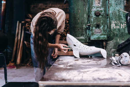 Portrait of young woman carefully work on a ceramic whale in workshop.