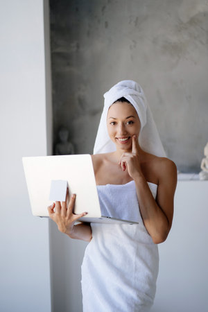 Woman freelancer in white towel stand in the bathroom with a laptopの写真素材