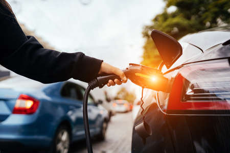 Woman near electric car. Vehicle charged at the charging station.