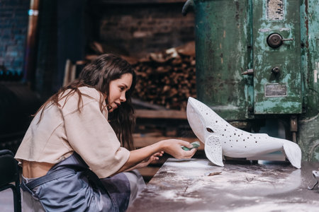 Portrait of young woman carefully work on a ceramic whale in workshop.の写真素材