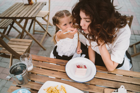 Young mom eating cake with smiling kid on the streetの写真素材