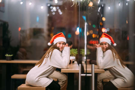 Girl wearing Santa Claus hat sitting in coffee shopの写真素材