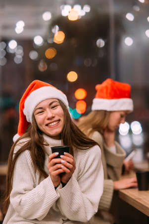 Girl wearing Santa hat sitting in coffee shop and drinking coffeeの写真素材