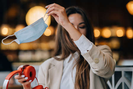 Girl in a cafe, takes off her protective medical face maskの写真素材