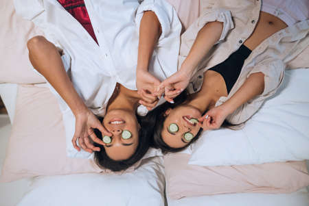 Home spa. Two women holding pieces of cucumber on their faces