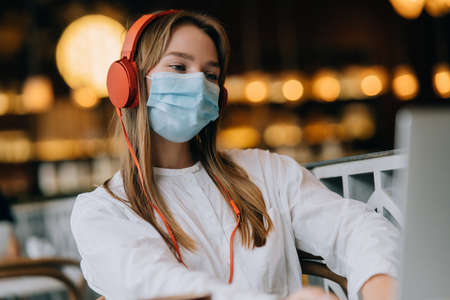 A girl sitting in a coffee shop with headphones. Coronavirus outbreak.の写真素材