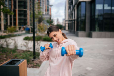 Young fitness girl making exercises with dumbbells in city parkの写真素材