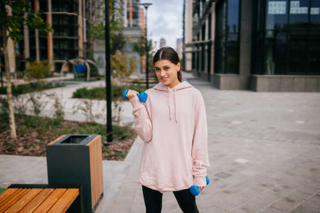 Young fitness girl making exercises with dumbbells in city parkの写真素材